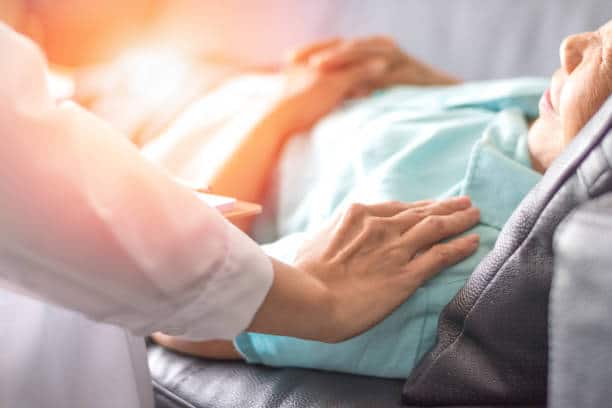 Femme tenant la main d'une femme âgée sur son lit d'hôpital où elle reçoit des soins palliatifs