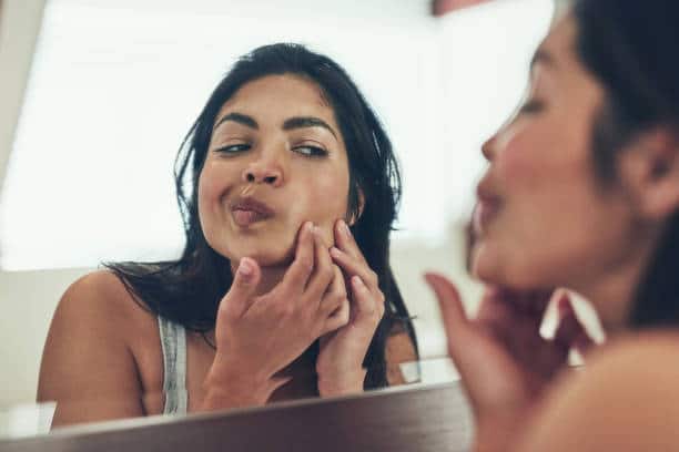 Femme retirant l'excès de sebum de sa peau grasse devant le miroir