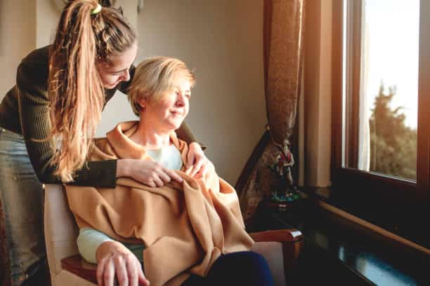 Jeune femme tenant par l'épaule une autre femme dans un fauteuil pendant qu'elle a un soin palliatif